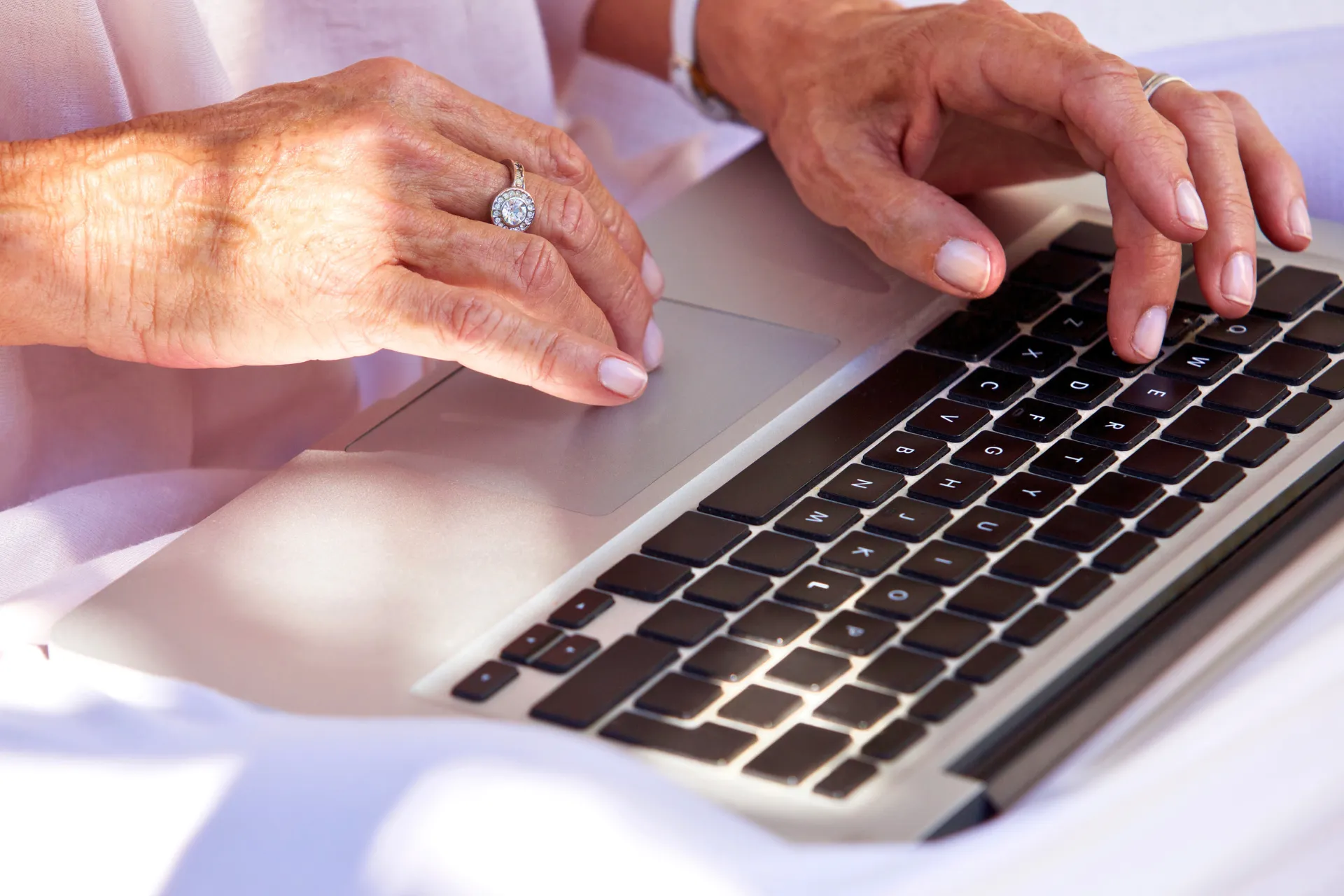 Close-up of elderly hands typing on a laptop keyboard, symbolizing legacy in a digital age