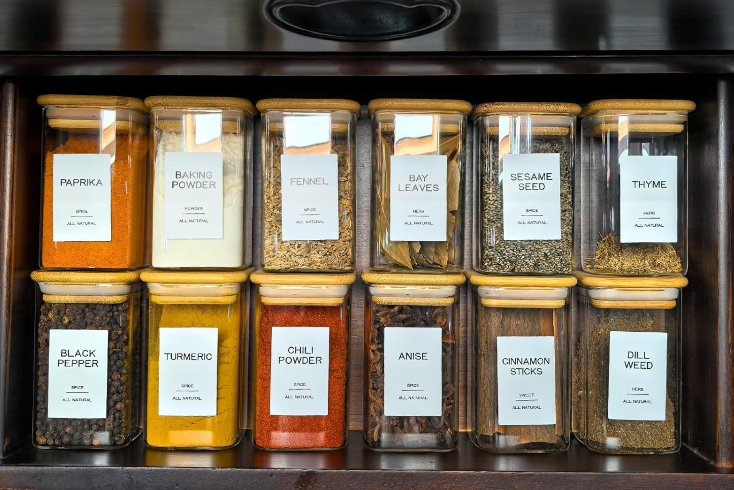 Set of labeled glass spice jars neatly organized in a kitchen spice rack, featuring paprika, turmeric, coriander, and other spices.